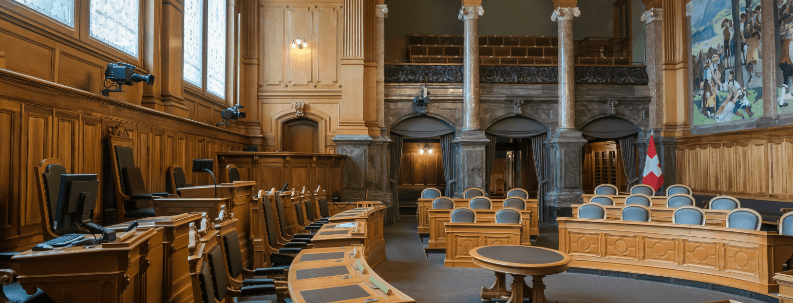Interior of a traditional courtroom with wooden paneling, marble columns and curved rows of desks